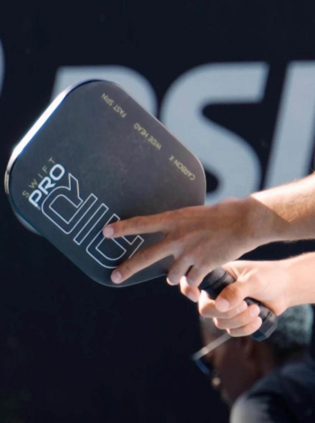 Person holding a pickleball paddle with 'Pro Paddle' branding against a dark background